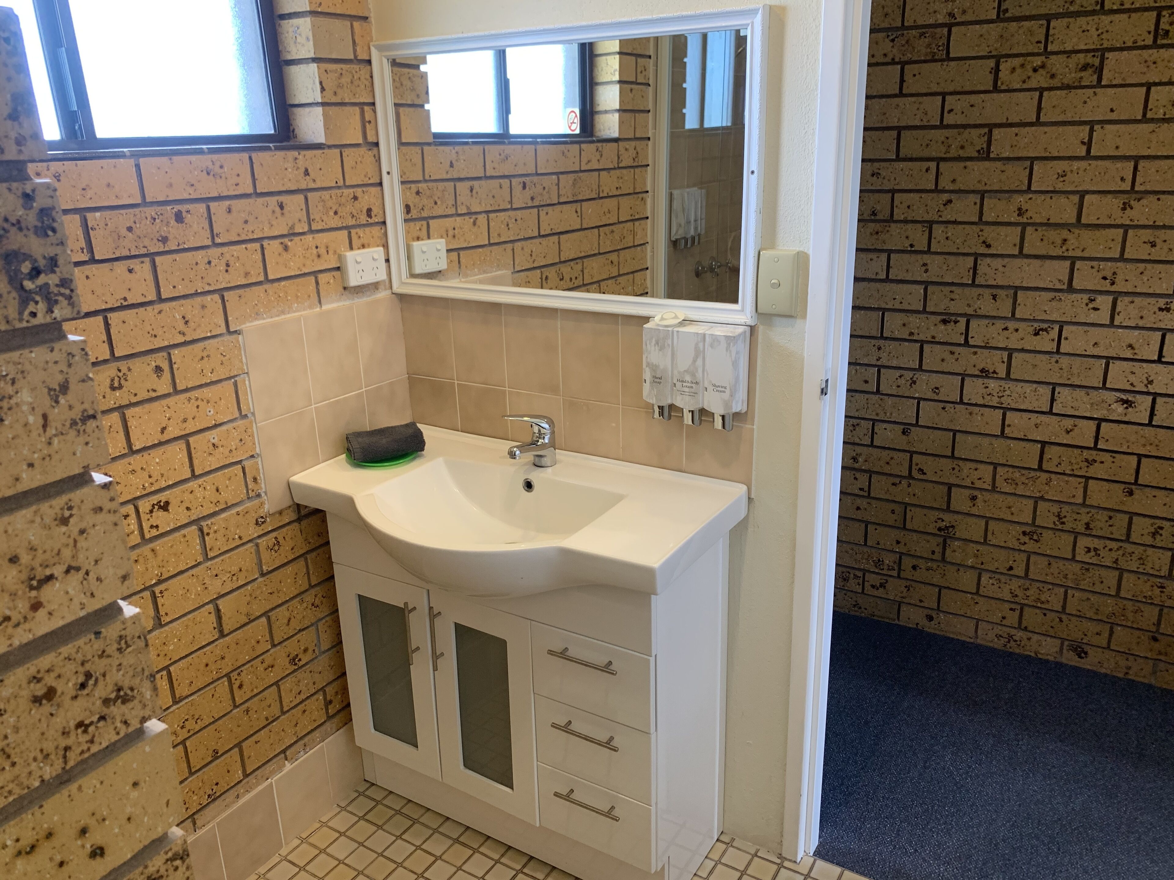 A bathroom with a white sink, a mirror, a towel rack, and a soap dispenser.