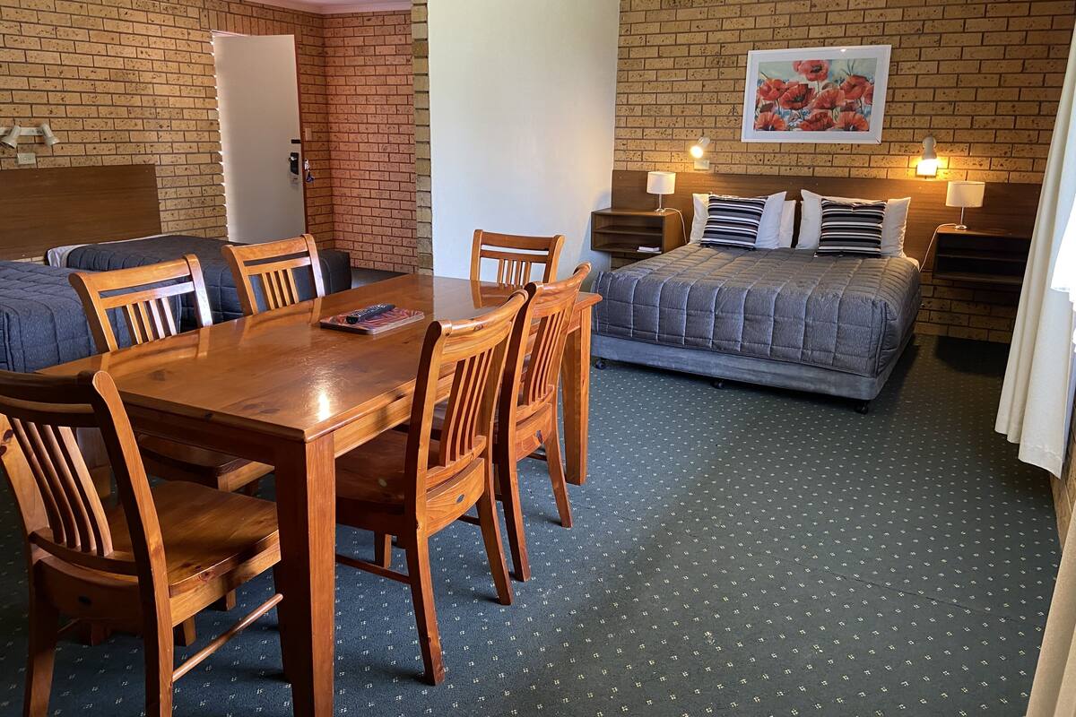 A room with a dining table and chairs, a bed with a quilt, a brick wall, and a painting.