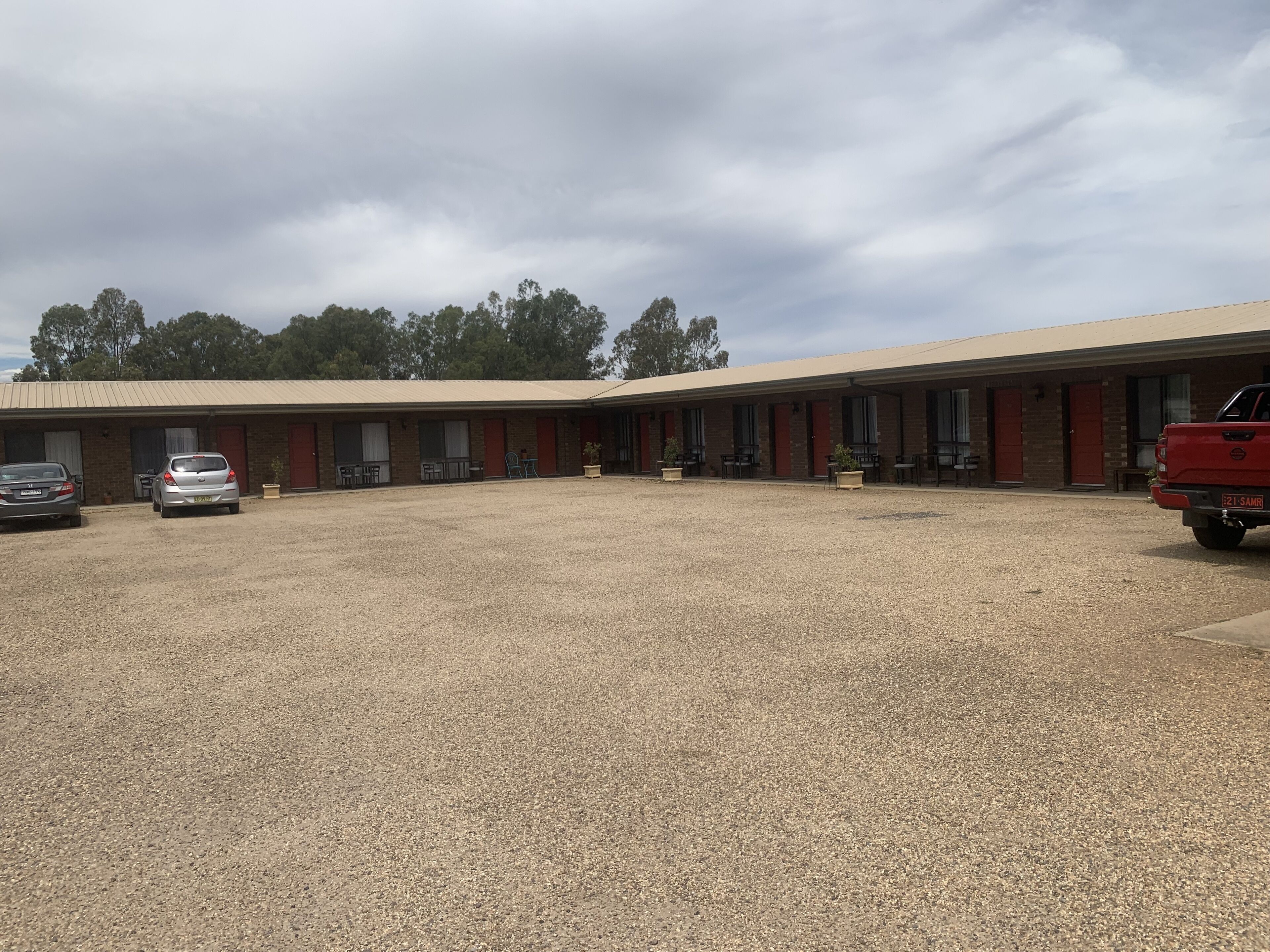 A motel with a gravel parking area, multiple rooms with red doors, and a red pickup truck parked in the lot.