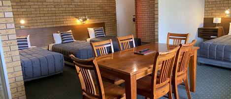 Habitación con dos camas, una mesa de comedor y sillas. Paredes de ladrillo y una lámpara en el techo.