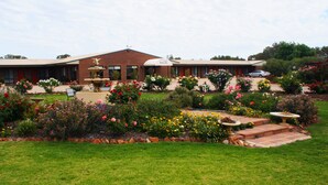 Een hotel met een bakstenen gevel, een fontein en een verzorgde tuin met diverse bloemen en struiken.
