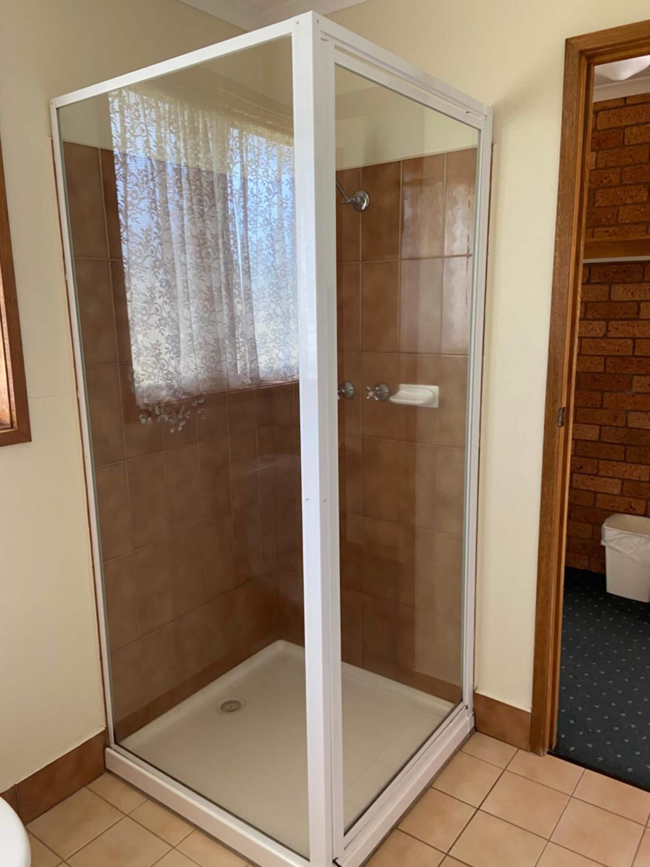A glass-enclosed shower room with a tiled floor and a wooden door frame.