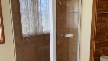 A glass-enclosed shower room with a tiled floor and a wooden door frame.