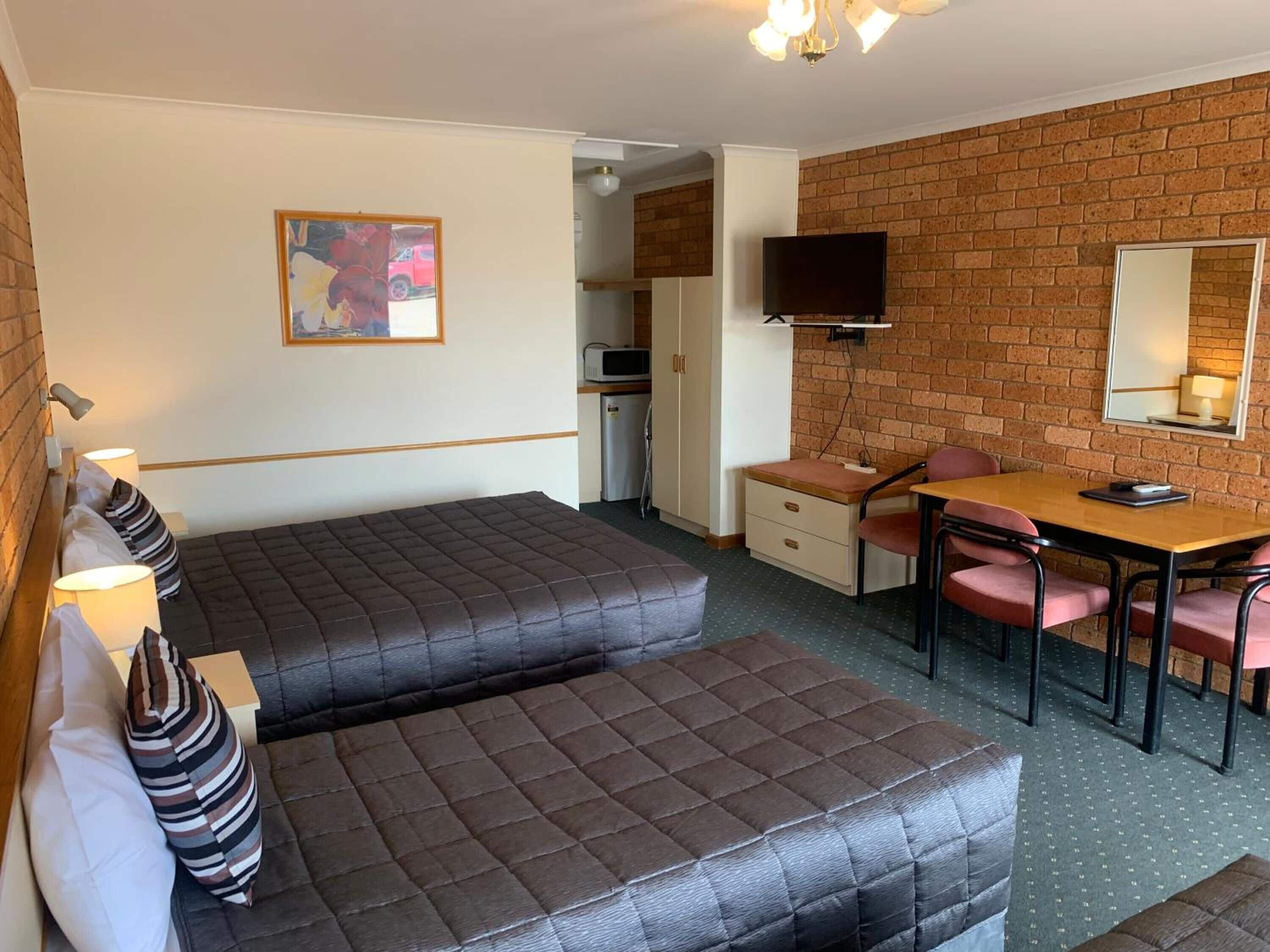 Ett hotellrum med två sängar, ett skrivbord, en stol, en tv och en vägg av tegelsten.