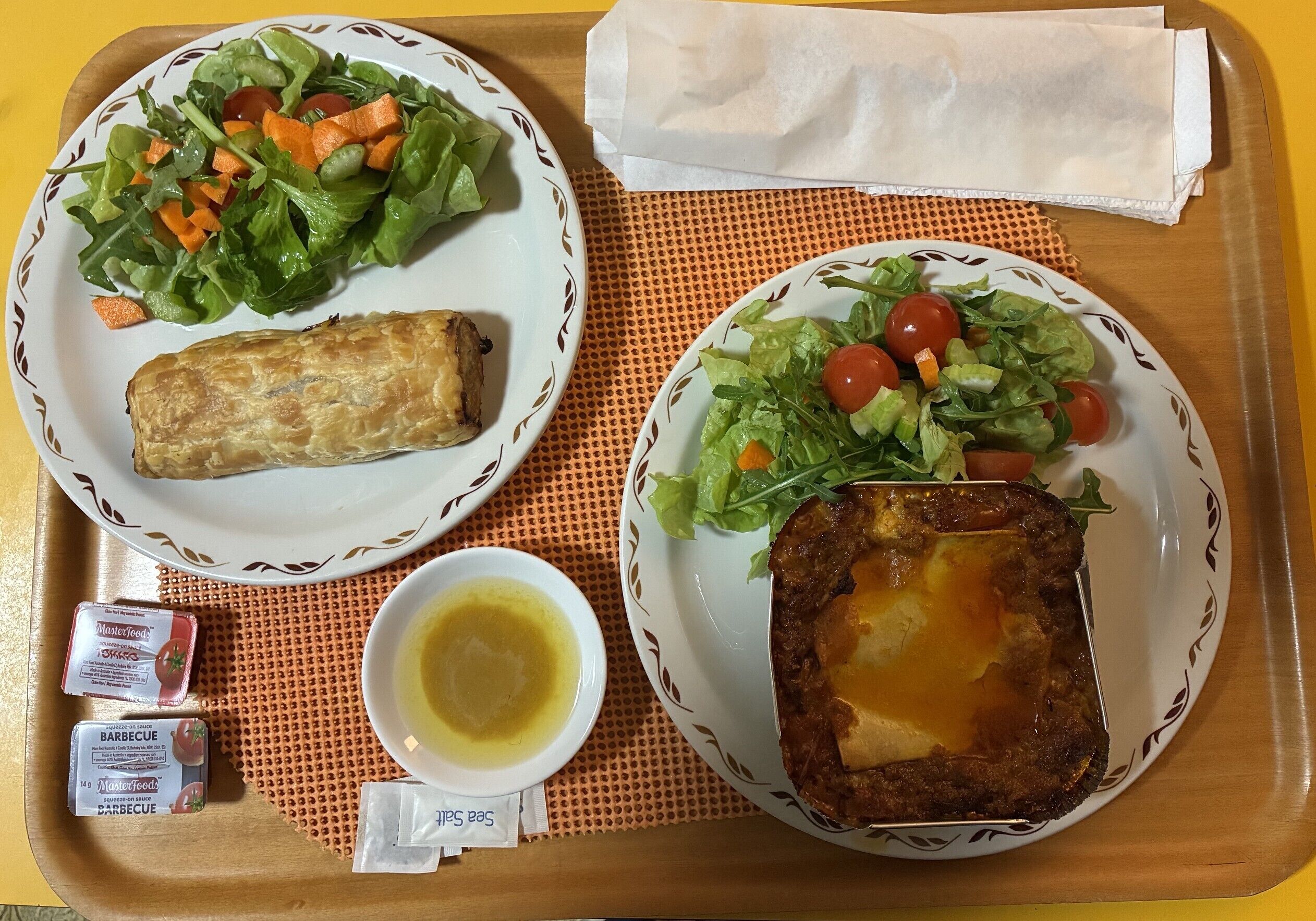 Two plates of food, a napkin, and condiments on a tray.