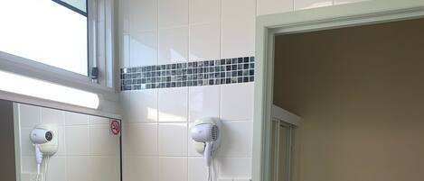 Un baño con un lavamanos blanco, dos espejos, un secador de pelo y una botella de champú.