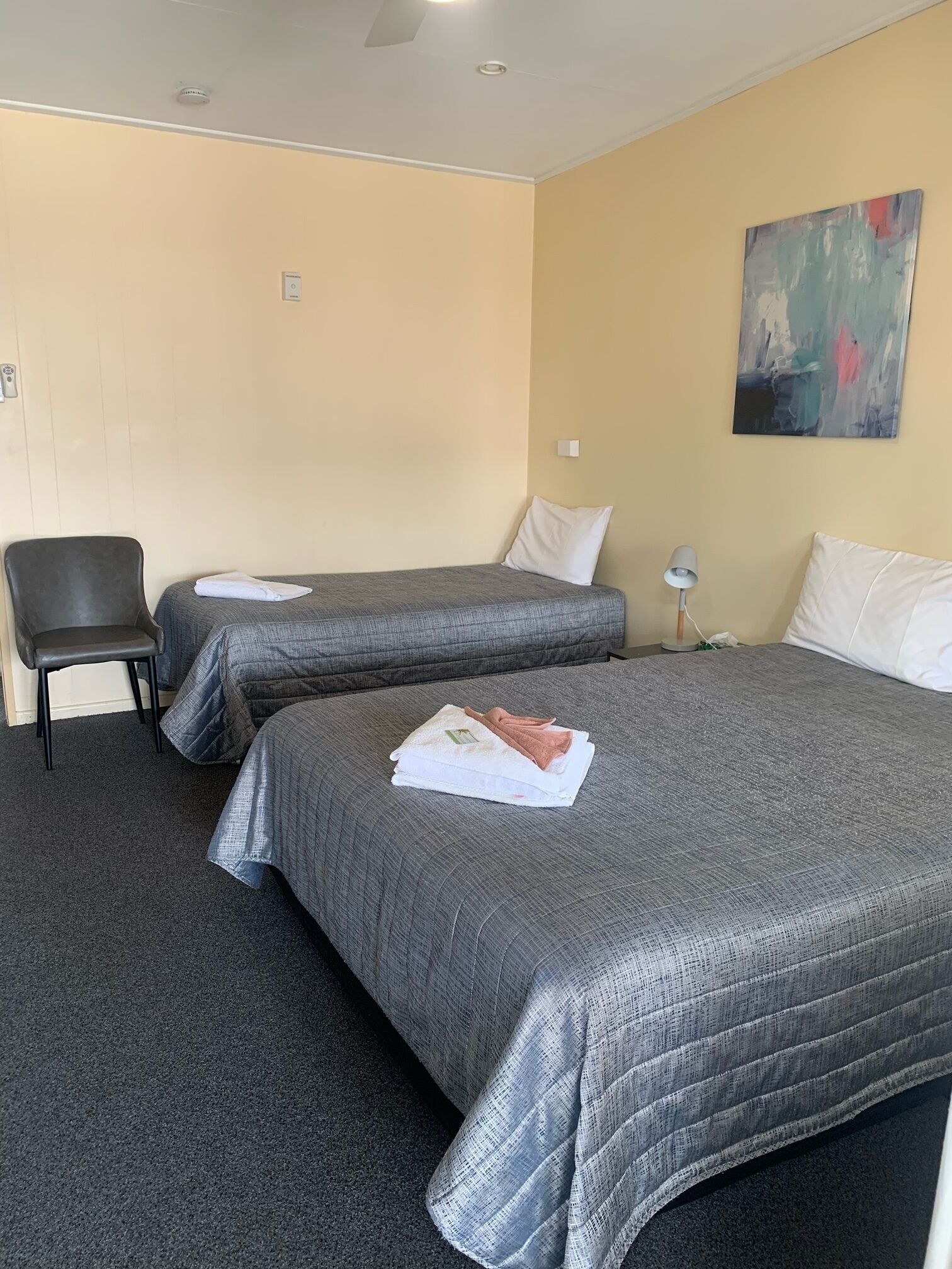 A hotel room with two beds, a chair, and a painting on the wall.