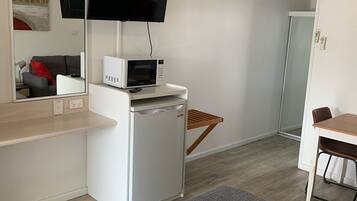 Een compacte hotelkamer met kitchenette, een flatscreen televisie boven de counter, een kleine koelkast en een magnetron.