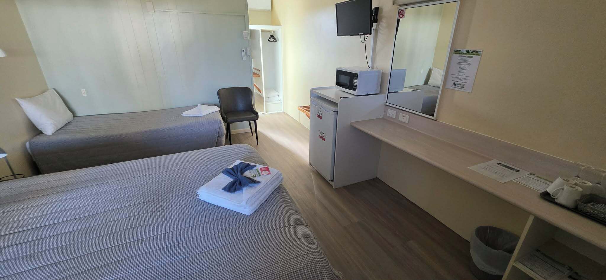 A hotel room with two beds, a desk with a microwave, a chair, a small trash bin, and a mirror on the wall.