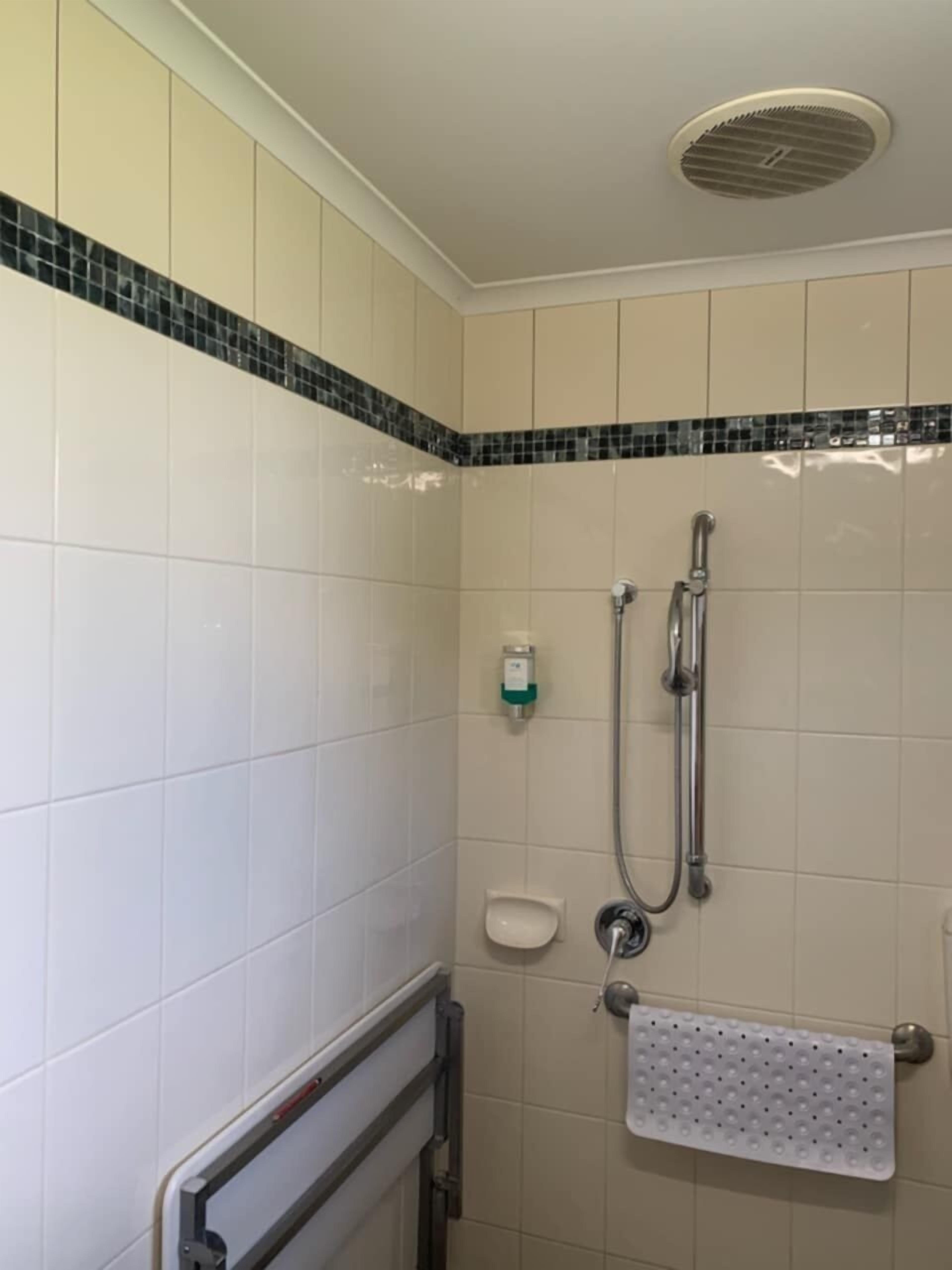 A shower area with a handheld showerhead, a handheld shower attachment, a soap dispenser, and a towel rack.