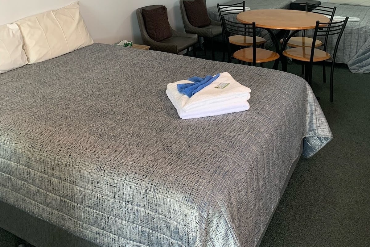 Habitació d'hotel amb llit, dues cadires, taula petita, ventilador de sostre i una obra d'art penjada a la paret.