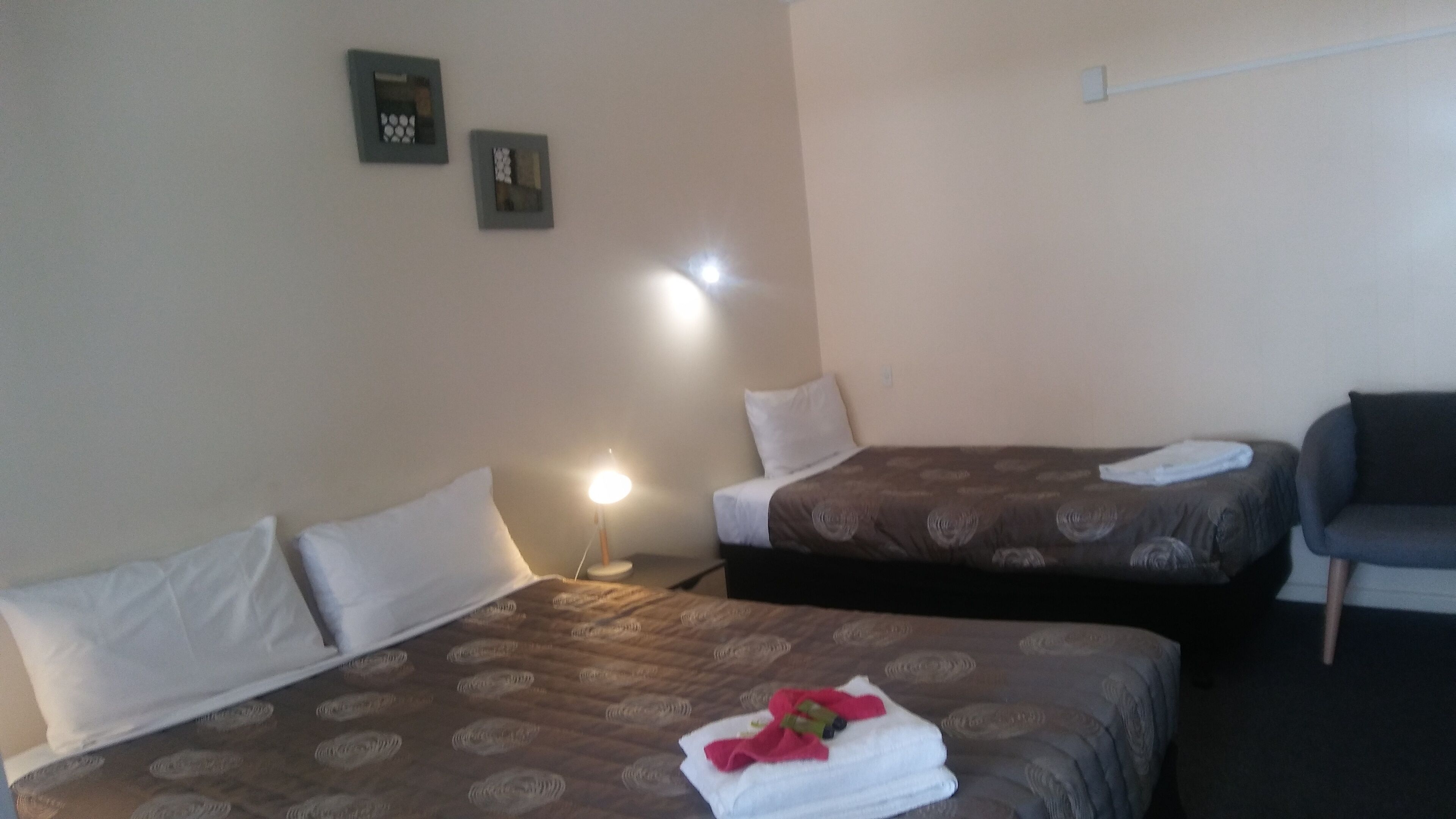 Una camera d'albergo con due letti, un comodino con lampada, un divano e due quadri appesi al muro.