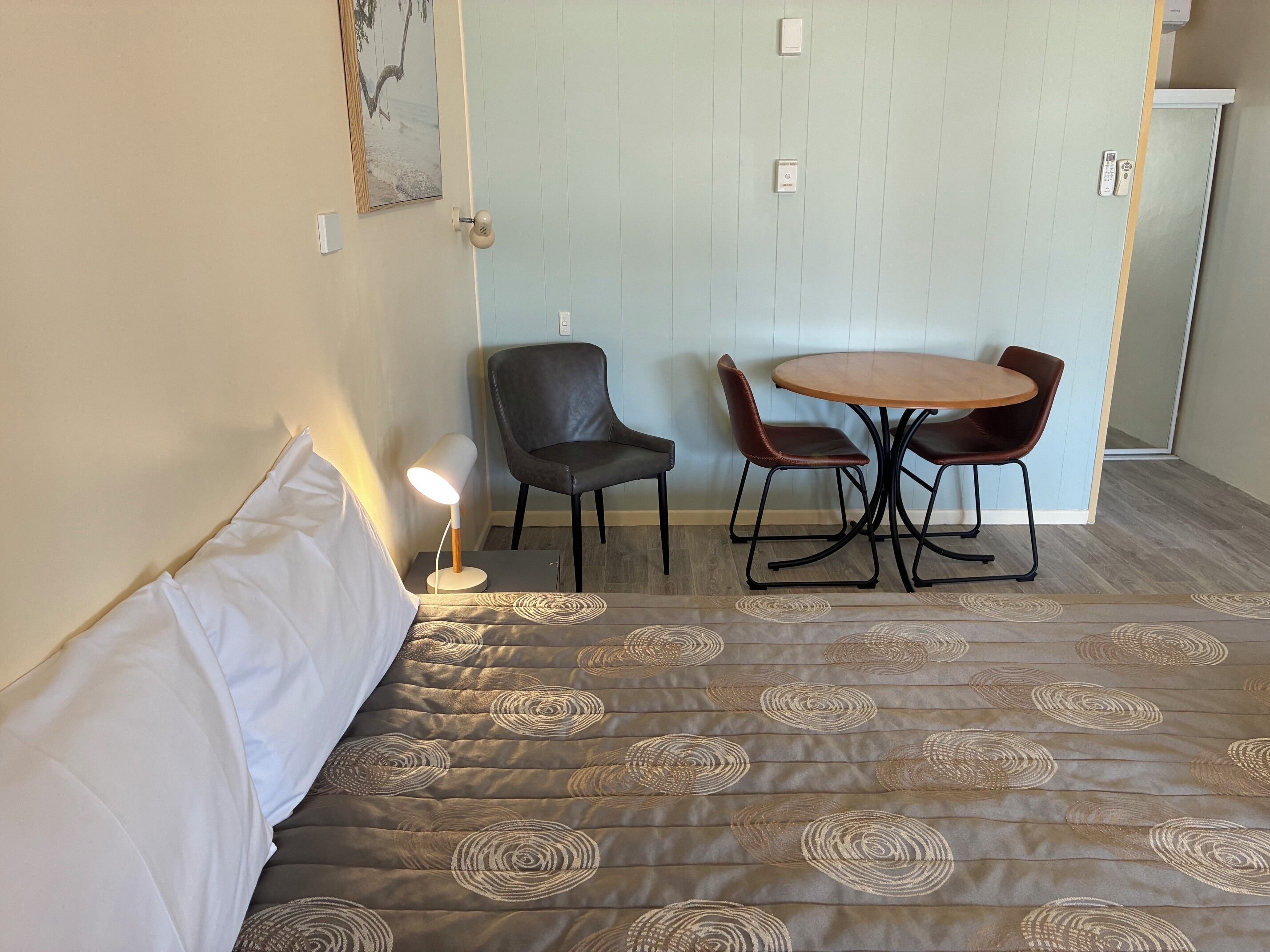 A room with a bed, a table with chairs, a lamp, and a door with a lock.
