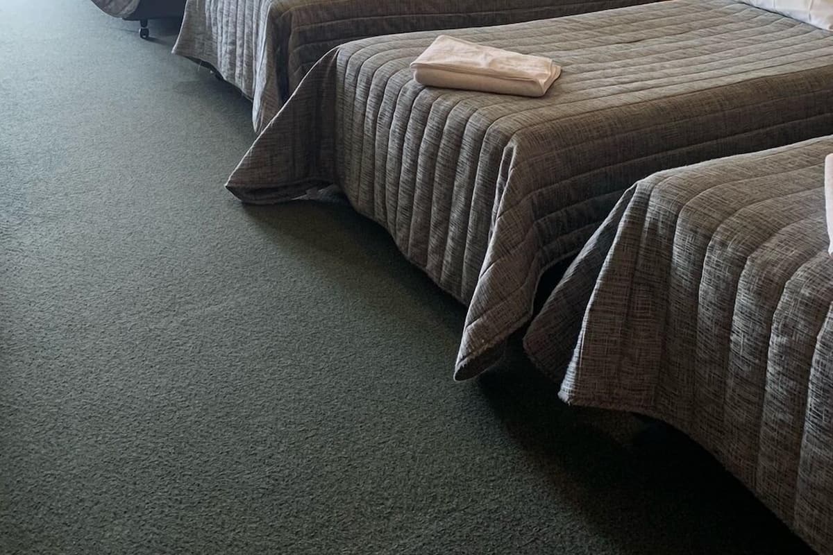 Habitació d'hotel amb quatre llits individuals, una paret de maó, un ventilador de sostre i una finestra amb cortines.