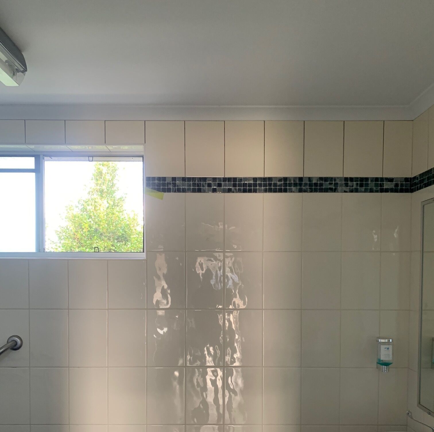 A bathroom with white tiled walls, a window, and a shower area.