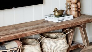 Een houten bank met gevlochten manden eronder, een boek met de titel 'The Flowers' en een stapel houten kommen op een wandplank.