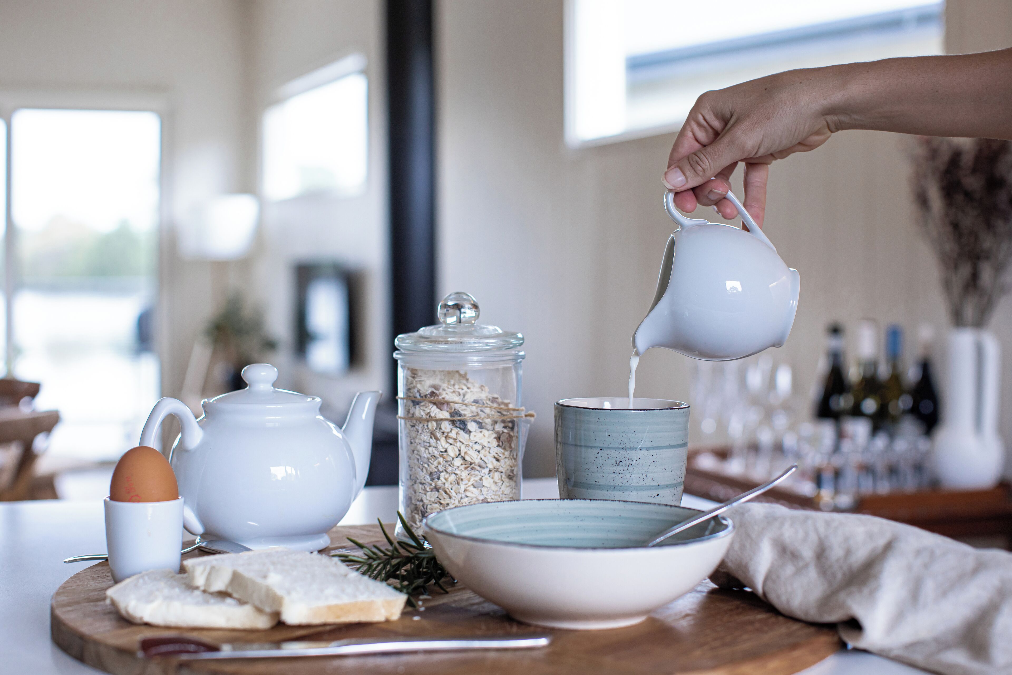 Une table de petit-déjeuner avec une théière, une tasse, un bol et un bocal de flocons d’avoine, le tout posé sur une planche en bois.