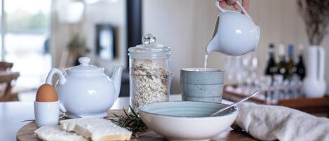 A breakfast setup with a teapot, a mug, a bowl, and a jar of oats on a wooden board.