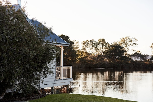 A lakeside house with a dock extending into the water, surrounded by trees and a clear sky.