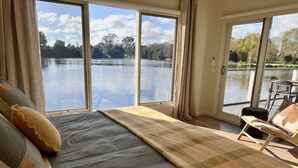 Een slaapkamer met een groot bed, uitzicht op een meer en een stoel bij het raam.