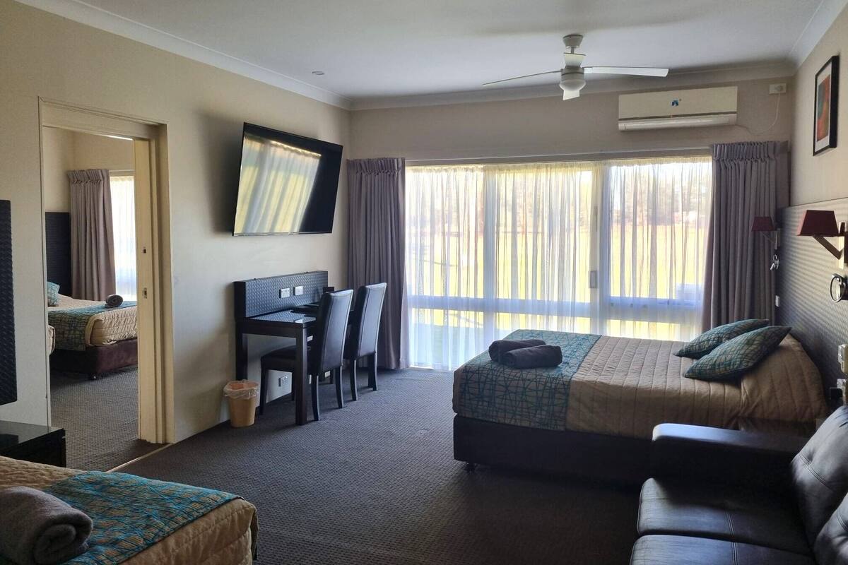A hotel room with a bed, a desk with chairs, a television, and a ceiling fan.