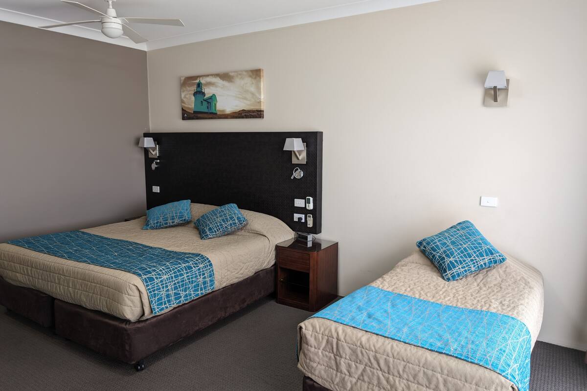 A hotel room with two beds, a ceiling fan, a painting, and a nightstand with a lamp.