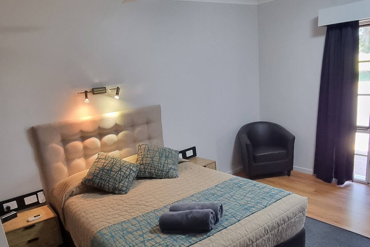 A neatly arranged bedroom with a bed, a chair, a ceiling fan, and a nightstand.