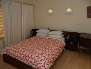 A neatly made bed with a patterned bedspread, a wooden headboard, two bedside lamps, and a small table with a chair. - Albion Motel Hotel (Castlemaine)