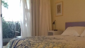 A bedroom with a bed, a nightstand, a lamp, and a window with curtains. - Albion Motel Hotel (Castlemaine)