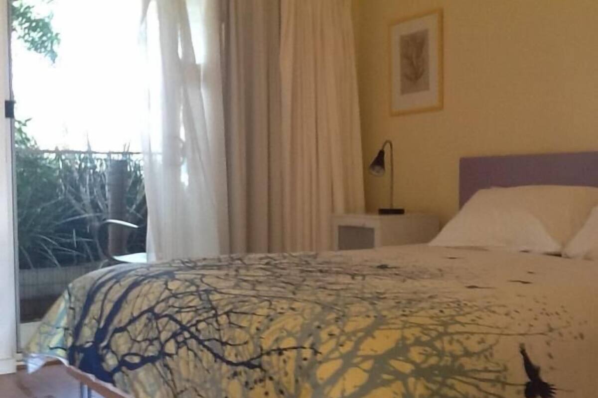 A bedroom with a bed, a nightstand, a lamp, and a window with curtains.