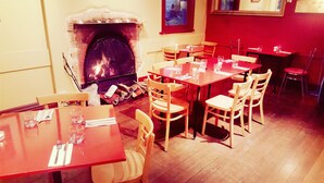 A restaurant with wooden tables and chairs, a brick fireplace, and a red wall. - Albion Motel Hotel (Castlemaine)
