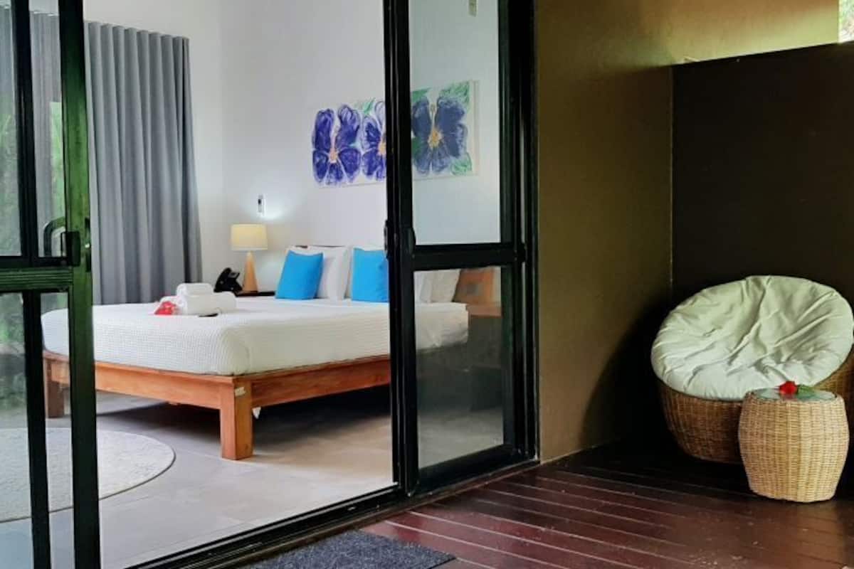 Een slaapkamer met een bed, een nachtkastje, een lamp en twee rieten stoelen.