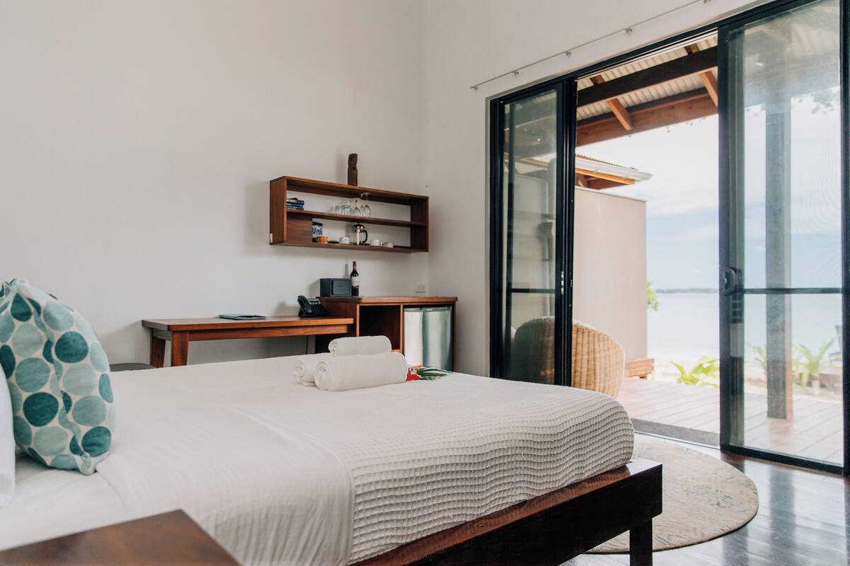 Een moderne slaapkamer met een groot bed, een bureau en uitzicht op zee door een schuifglazen deur.
