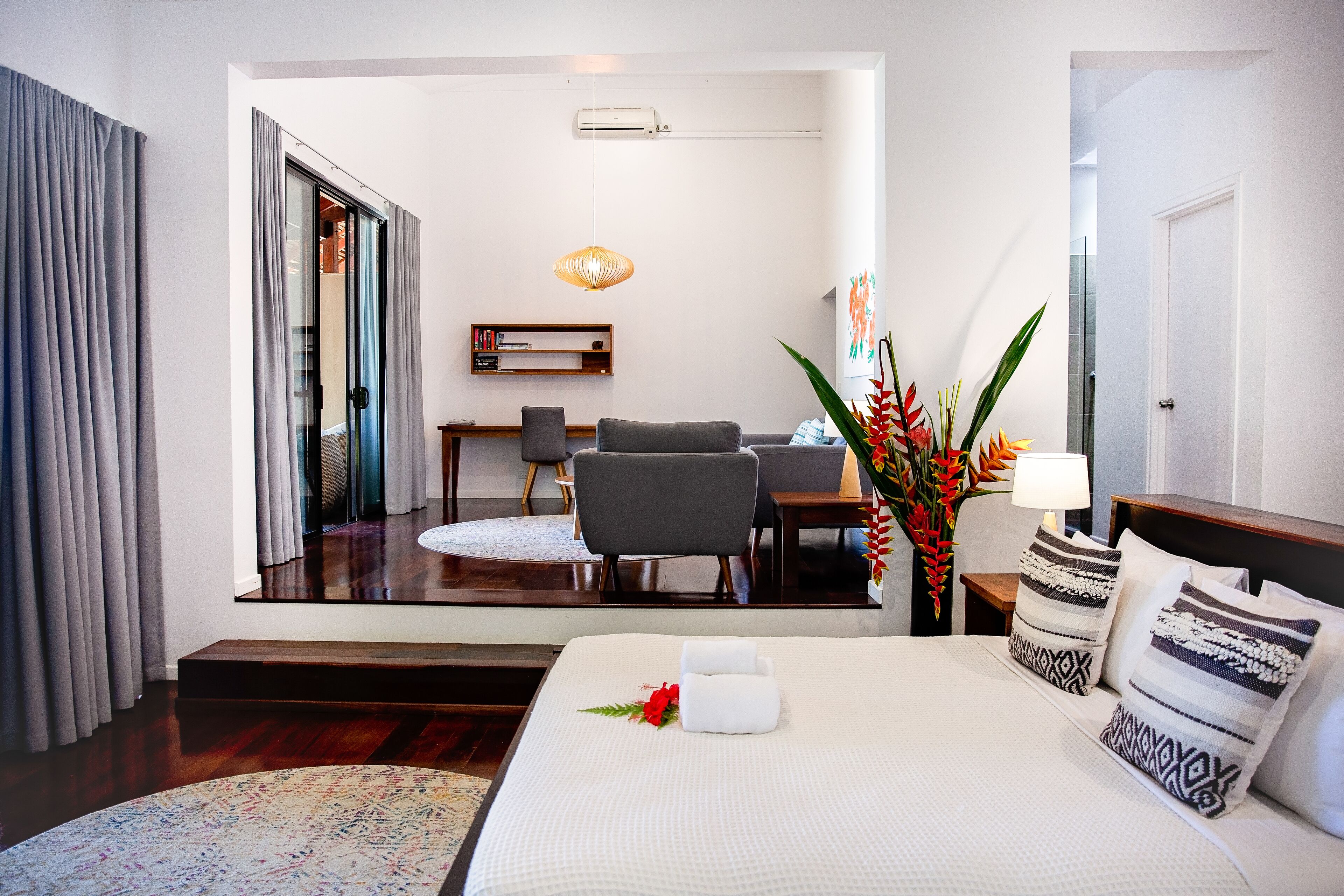 A hotel room with a bed, a desk, a chair, a mirror, and a plant.