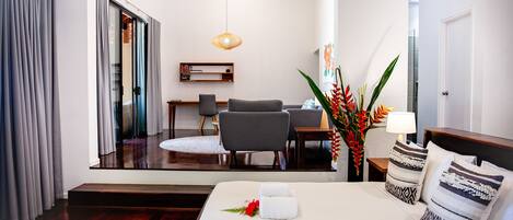 A hotel room with a bed, a desk, a chair, a mirror, and a plant.