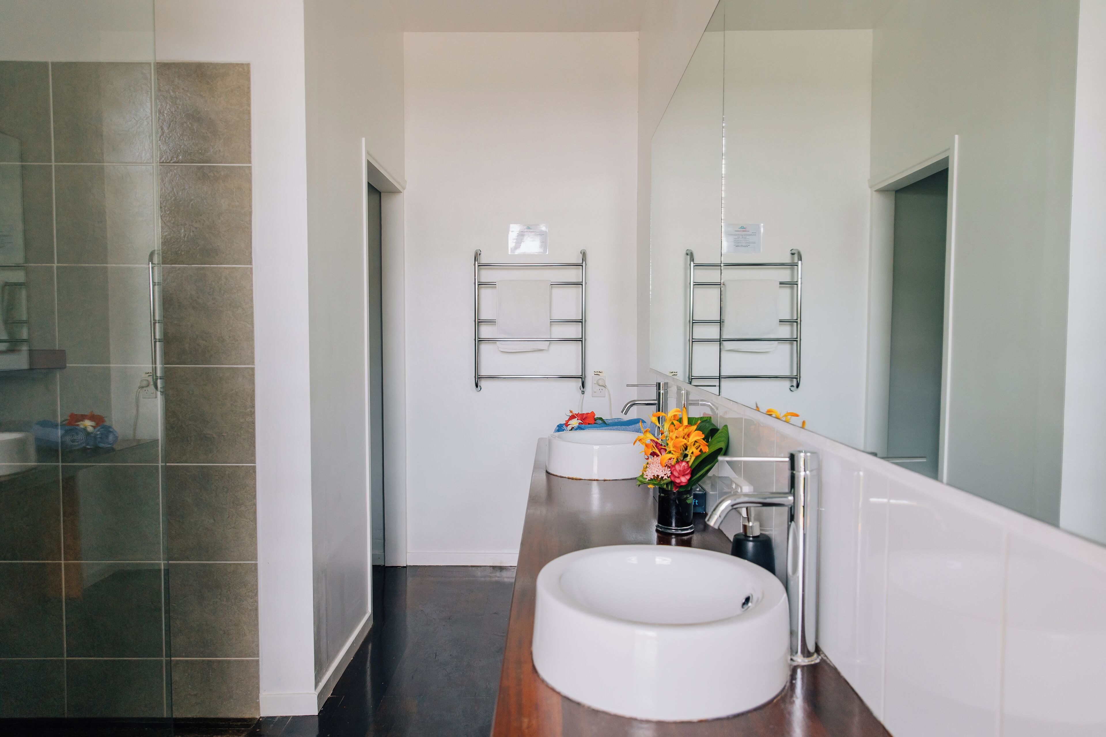 A modern bathroom with a glass shower enclosure, a white sink with a wooden countertop, and a large mirror.