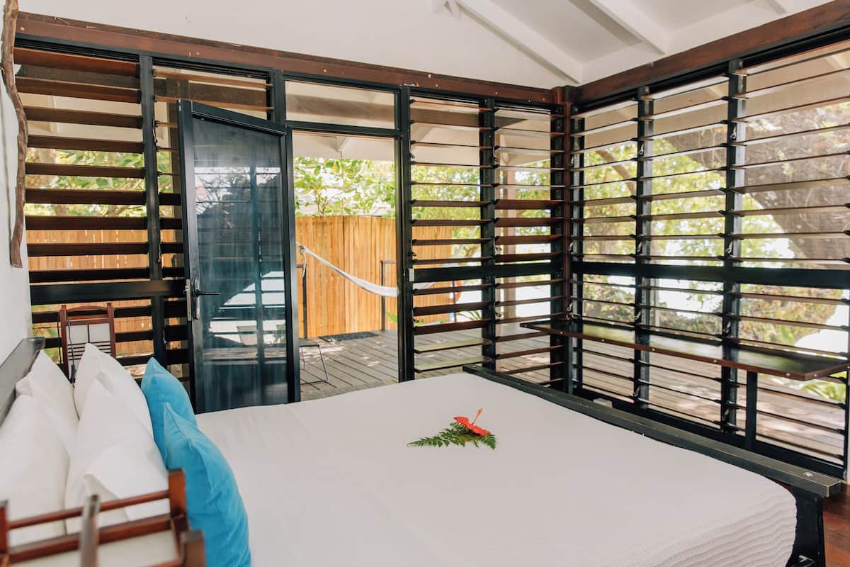 Een slaapkamer met een bed, een houten hoofdeinde en uitzicht door een raam met jaloezieën.
