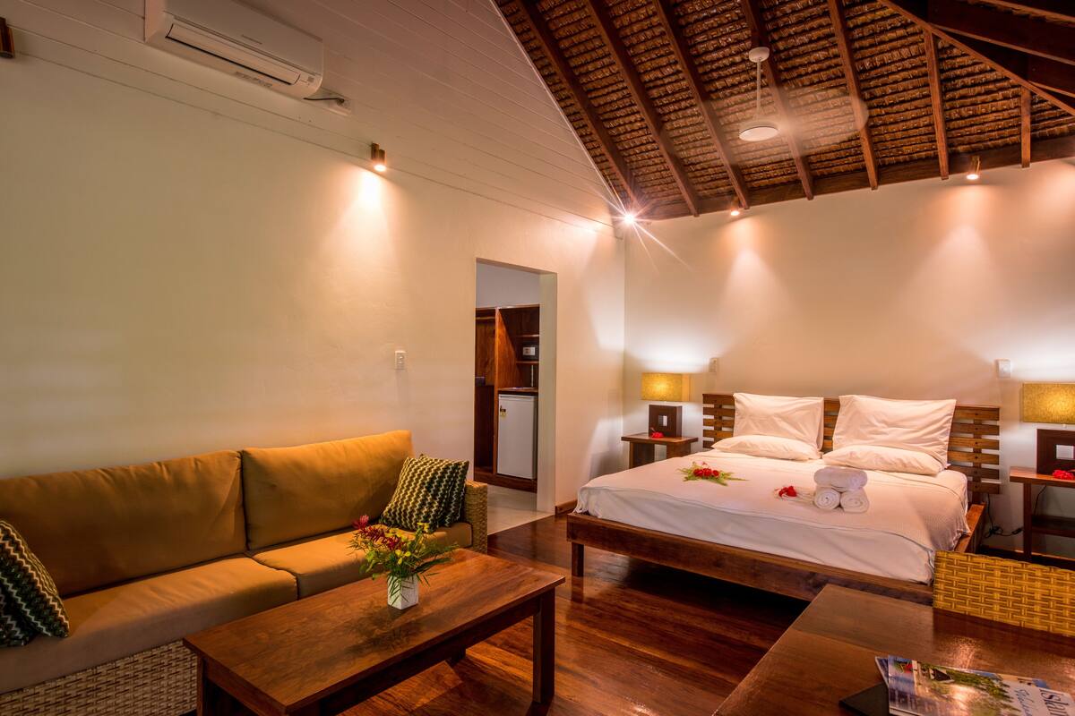 Een gezellige hotelkamer met een houten plafond, een bed met witte lakens, een bank, een bijzettafeltje en een kleine tafel met een bloevas.