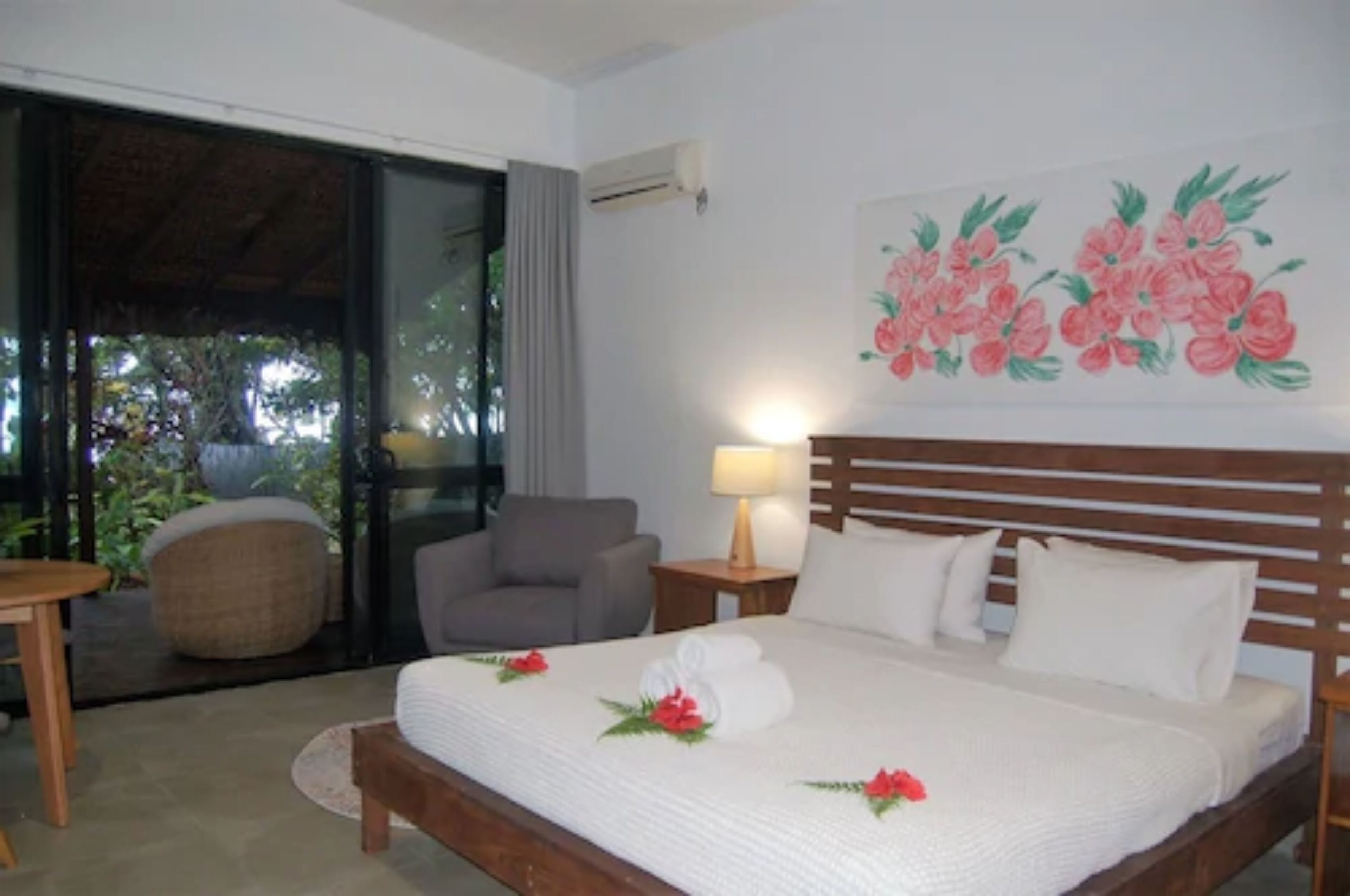 A hotel room with a bed, a chair, a table, and a view of the outdoors.