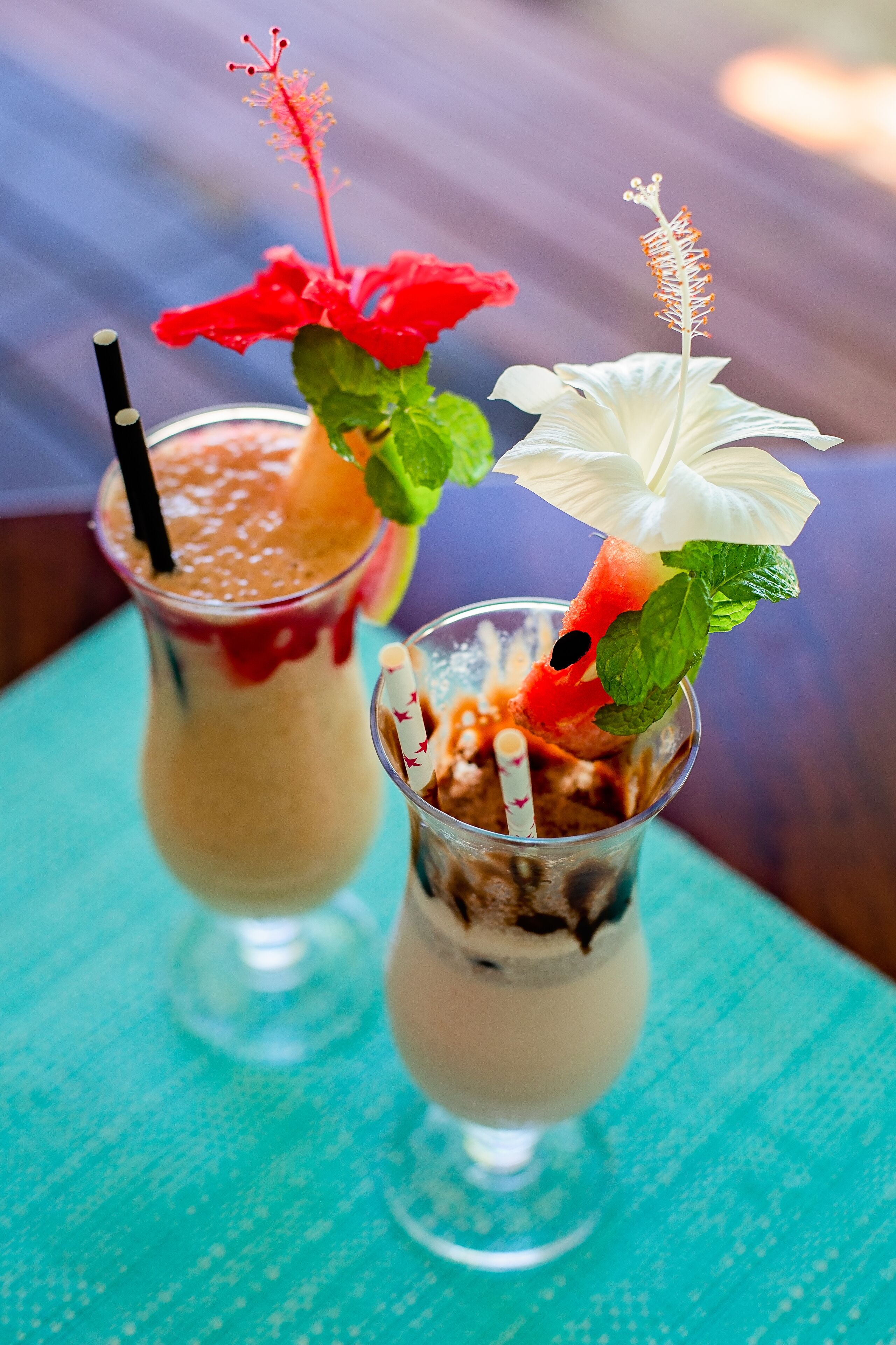Two drinks with fruit garnishes on a teal tablecloth.