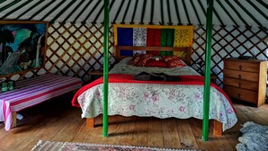 Interior d'una iurta tradicional amb un llit, una taula petita i un armari de fusta.