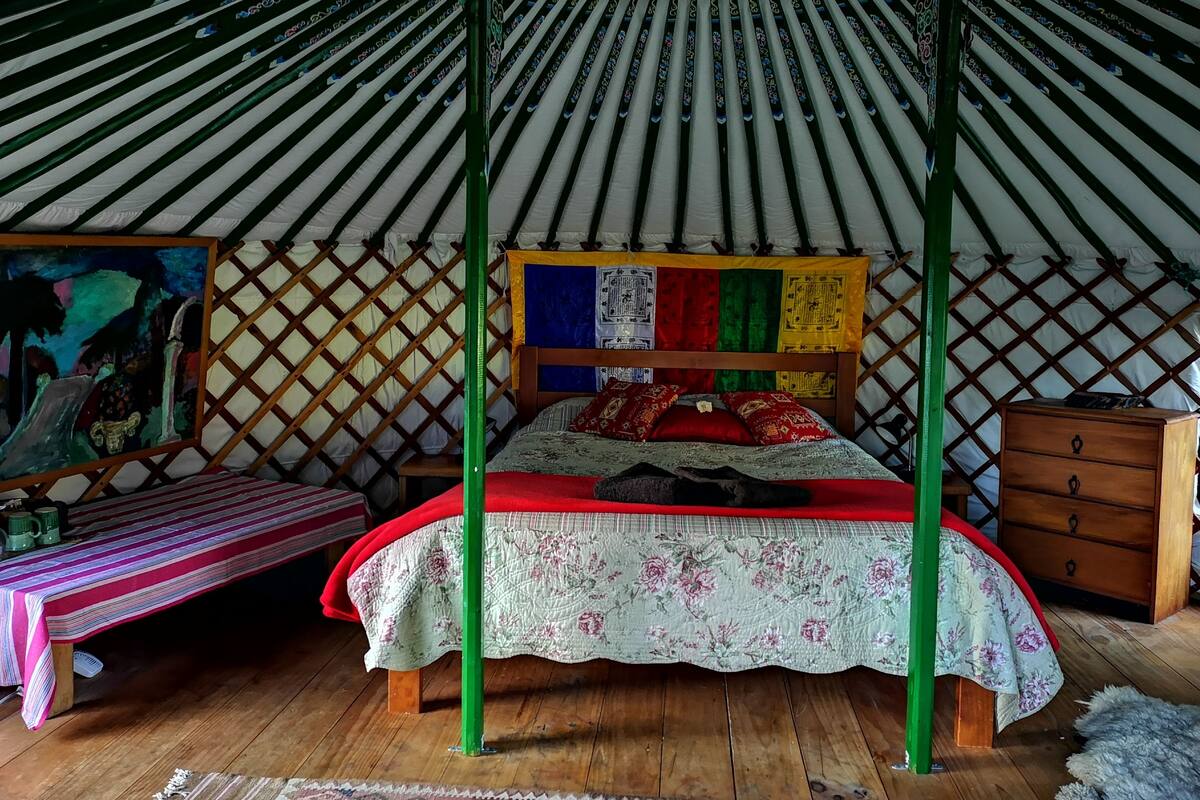 A traditional yurt interior with a bed, a small table, and a wooden cabinet.