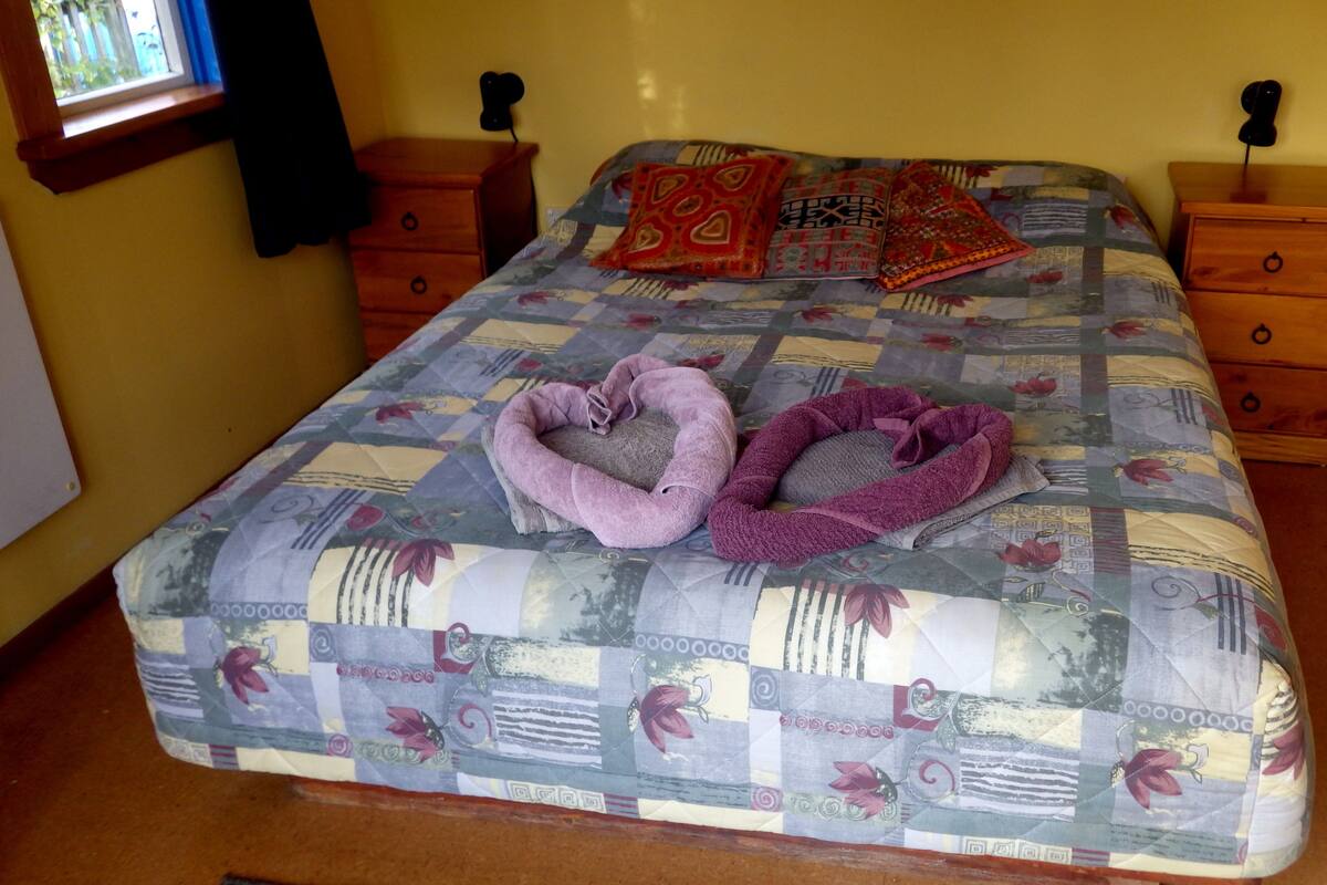 A bed with a quilted bedspread, two heart-shaped towels, and two pillows.