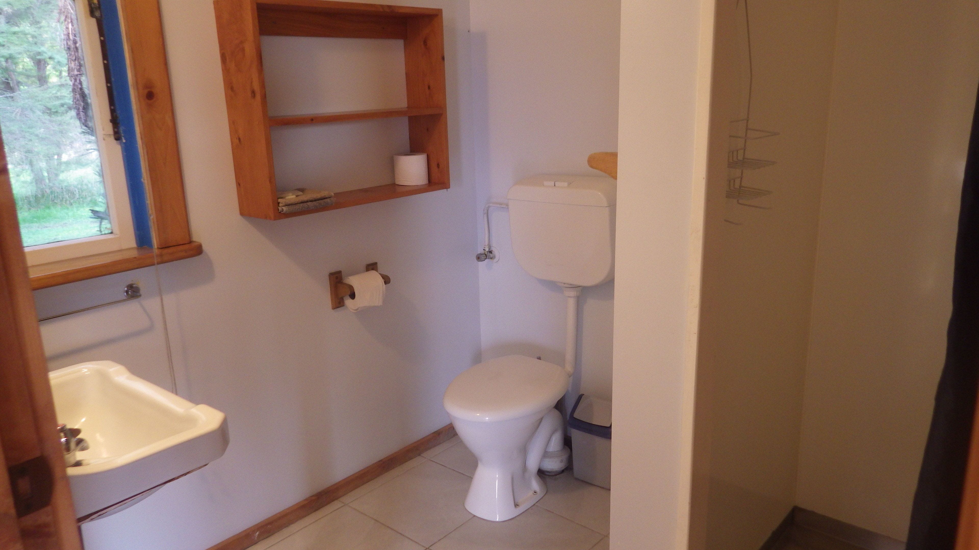 A small, clean bathroom with a toilet, a sink, and a shelf above the toilet.