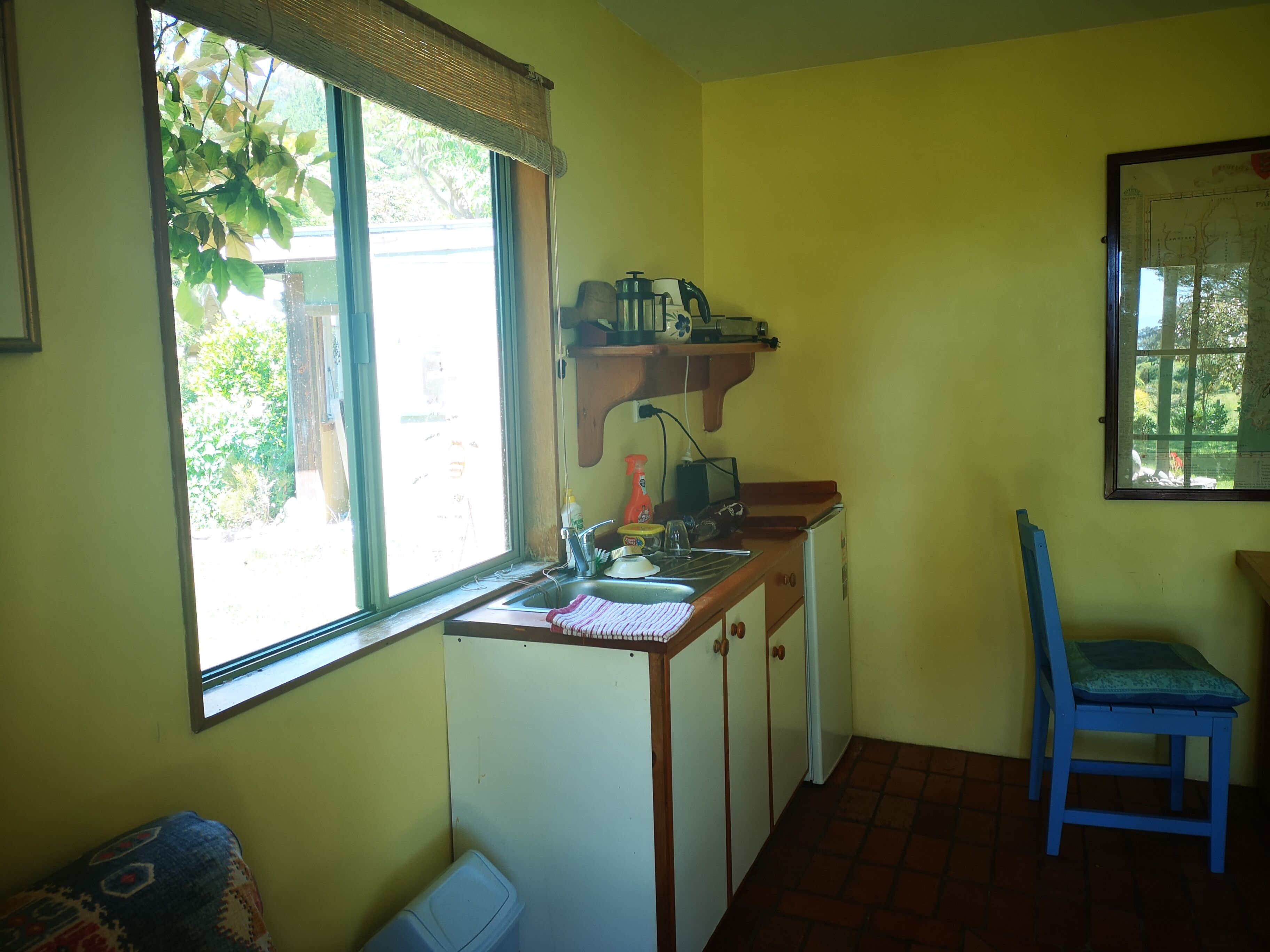 A compact kitchen with a window, a sink, a small refrigerator, and a chair.
