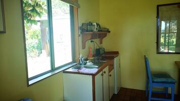 A compact kitchen with a window, a sink, a small refrigerator, and a chair.