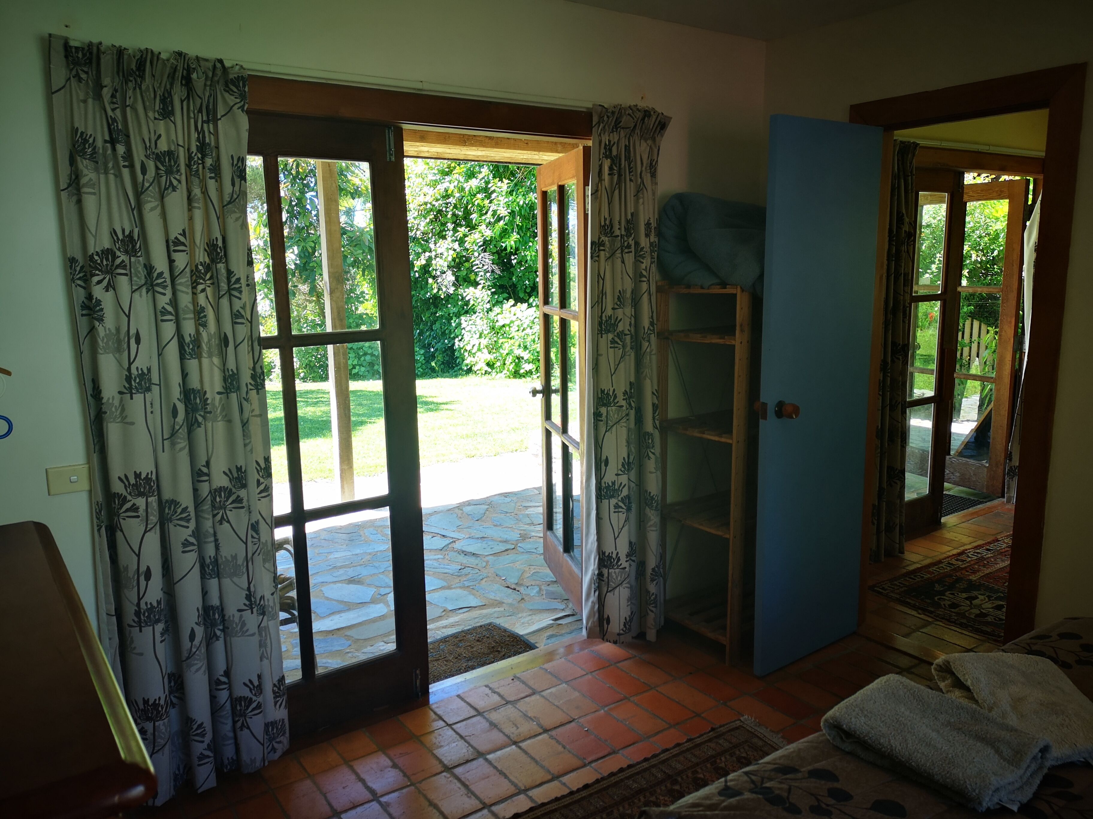 An open door leading to a stone-tiled patio with a view of greenery. A blue wall and a wooden shelf are visible inside.