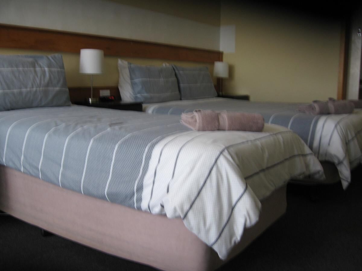 A hotel room with three beds, each with a headboard, pillows, and a blanket.