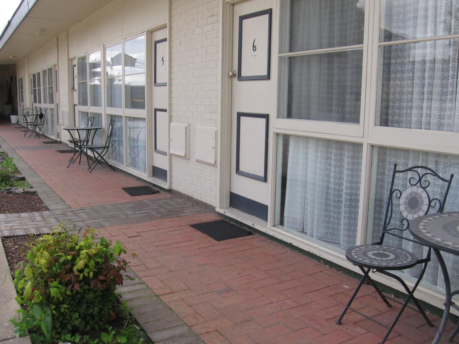 A row of rooms with numbered doors, a brick pathway, and outdoor seating.