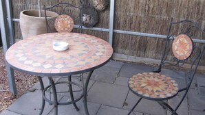Una mesa redonda para exteriores con diseño de mosaico, dos sillas de metal con respaldos coordinados y una maceta grande.